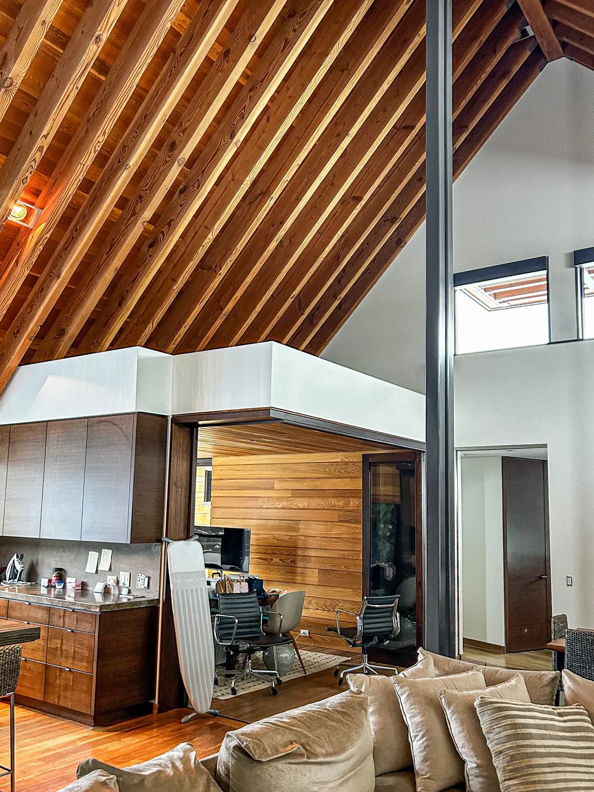 A cedar clad wall and exposed timber roof structure in a Clarksburg home, painted white above the kitchen and loft railing.