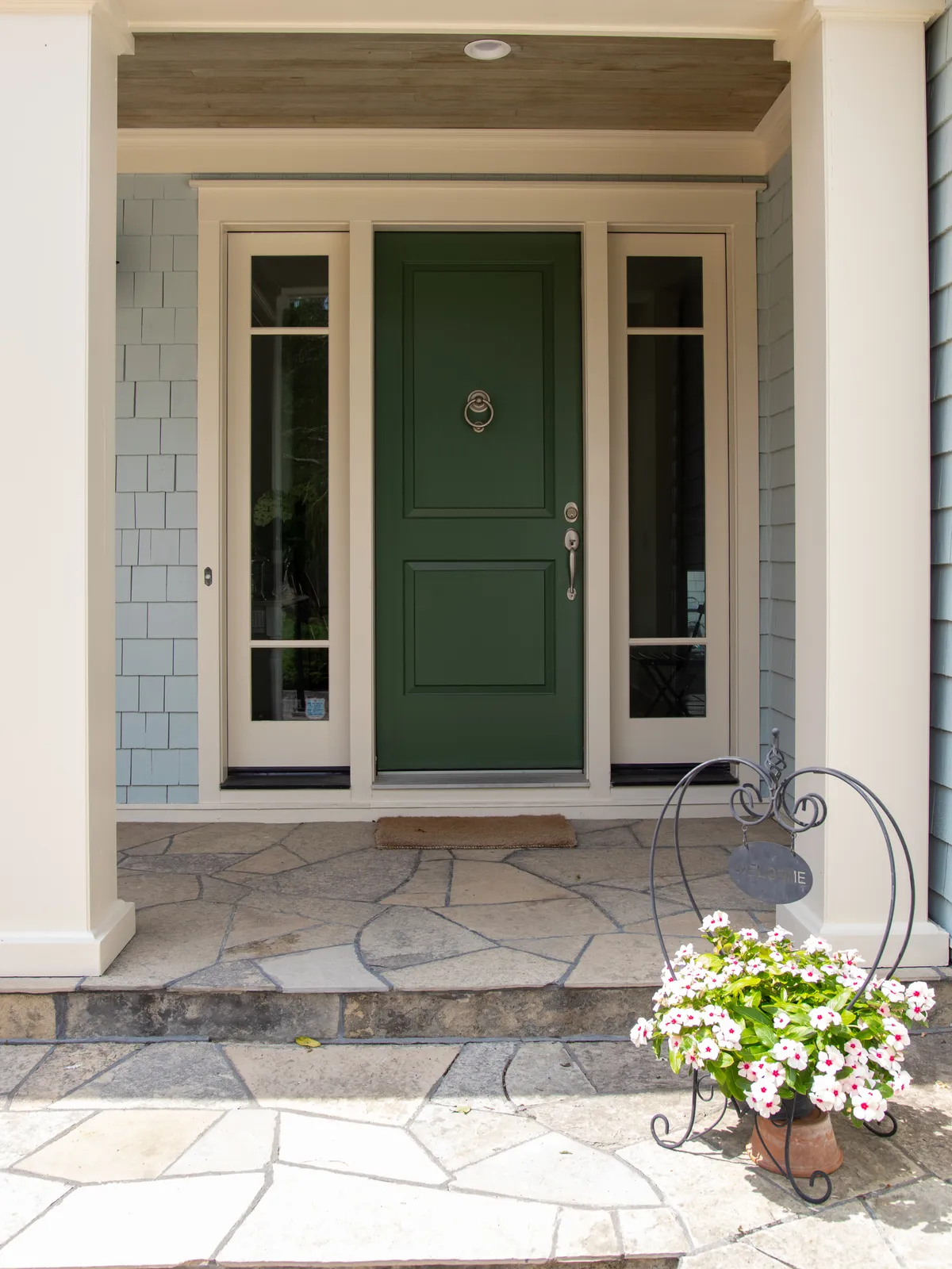 A deep green painted front door framed by sidelights and shingle siding, with planters on the flagstone step of a Creemore home.