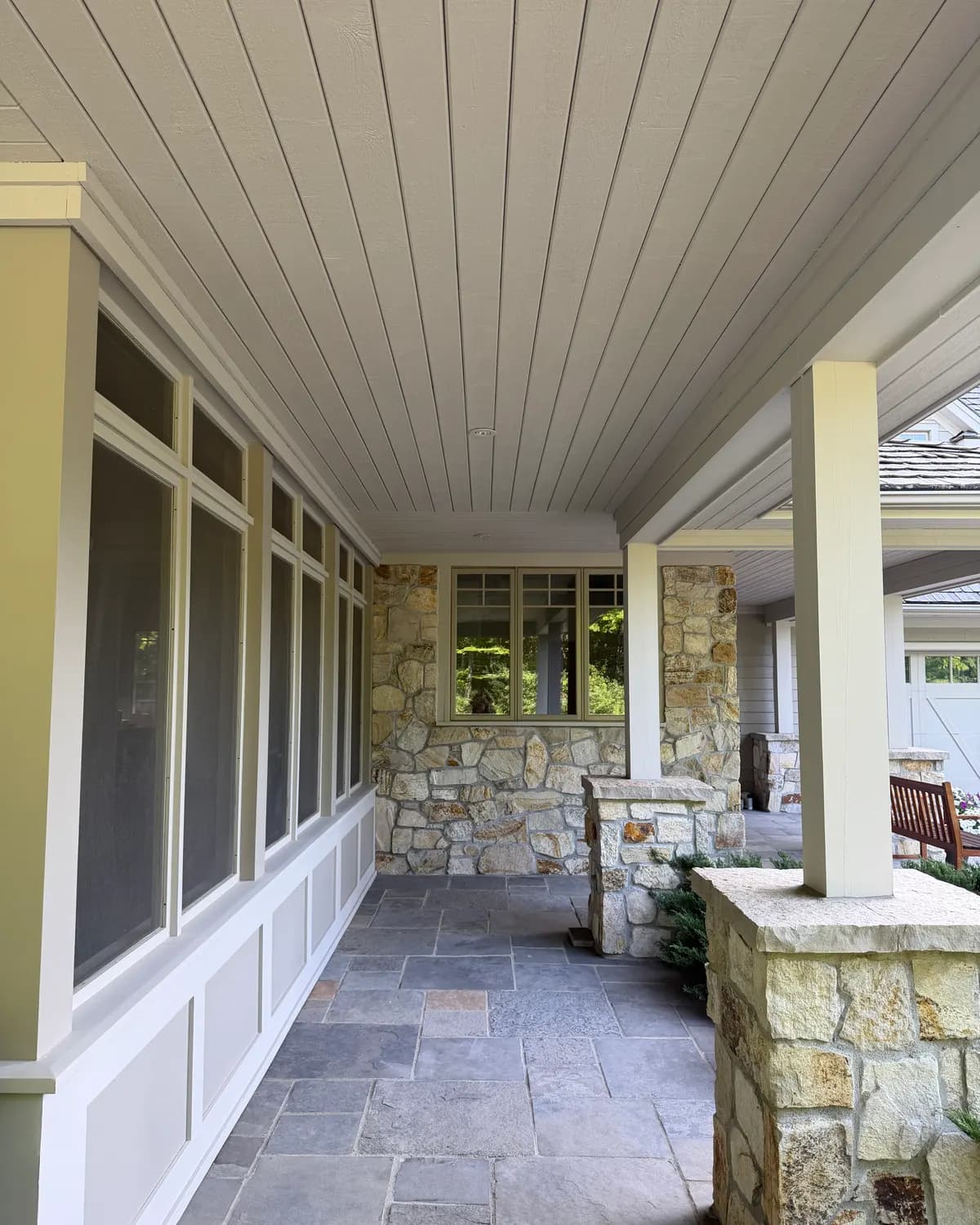 A covered porch in Craigleith with freshly painted posts and ceiling boards above a stone knee wall.