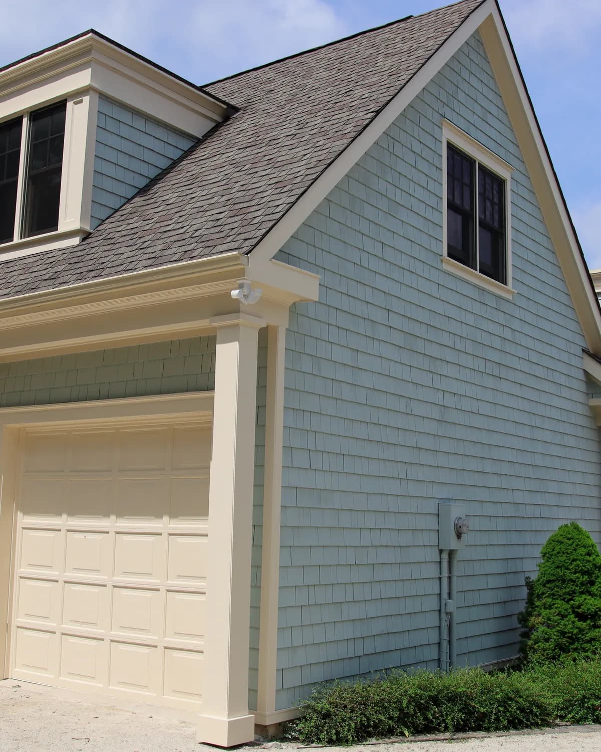 The gable and garage of a Creemore home, its cedar shakes stained pale sage with white trim.