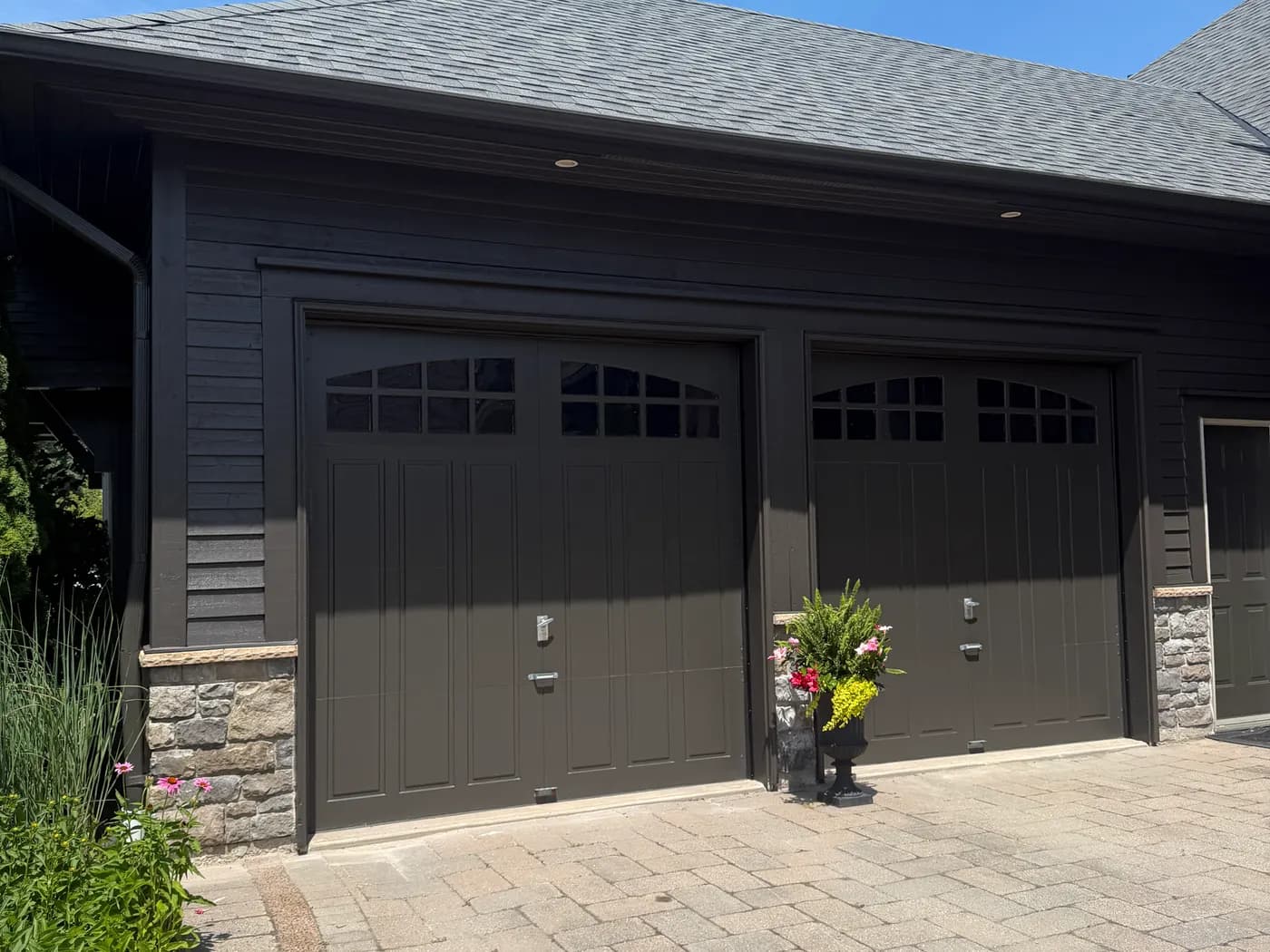 A pair of garage doors repainted deep charcoal to match the siding, with stone piers either side of the drive.