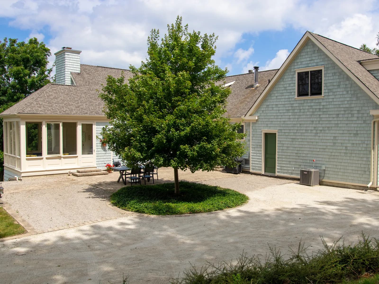 A sage green custom home in the hills of Creemore behind a broad shade tree, its trim and doors freshly painted.