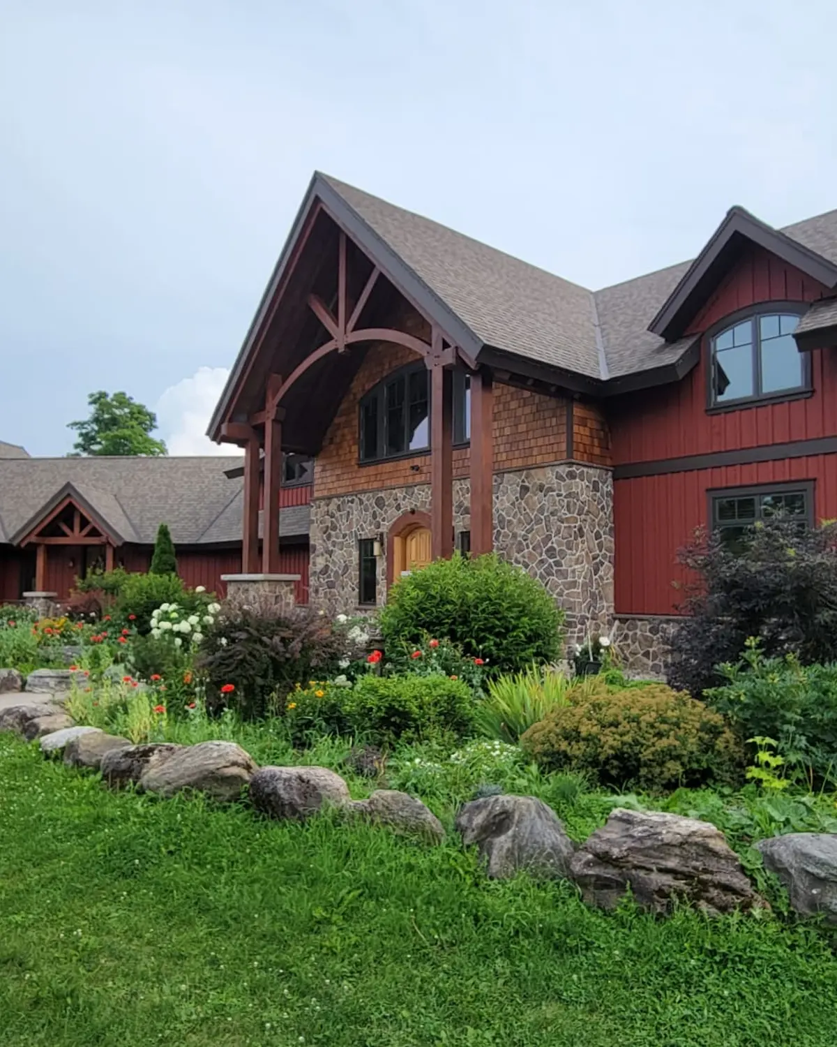 A timber frame home near Markdale in barn red, its stone base and heavy entry beams picked out against the planting.