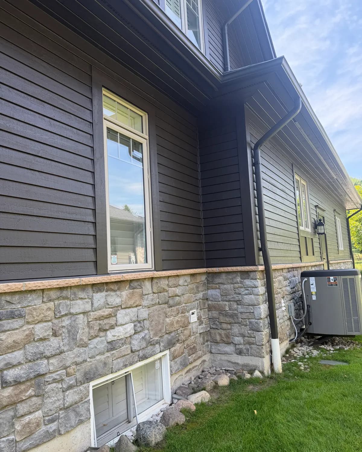 The side elevation of the Lora Bay home in Thornbury, siding and window frames carried in the same deep colour down to the stone base.