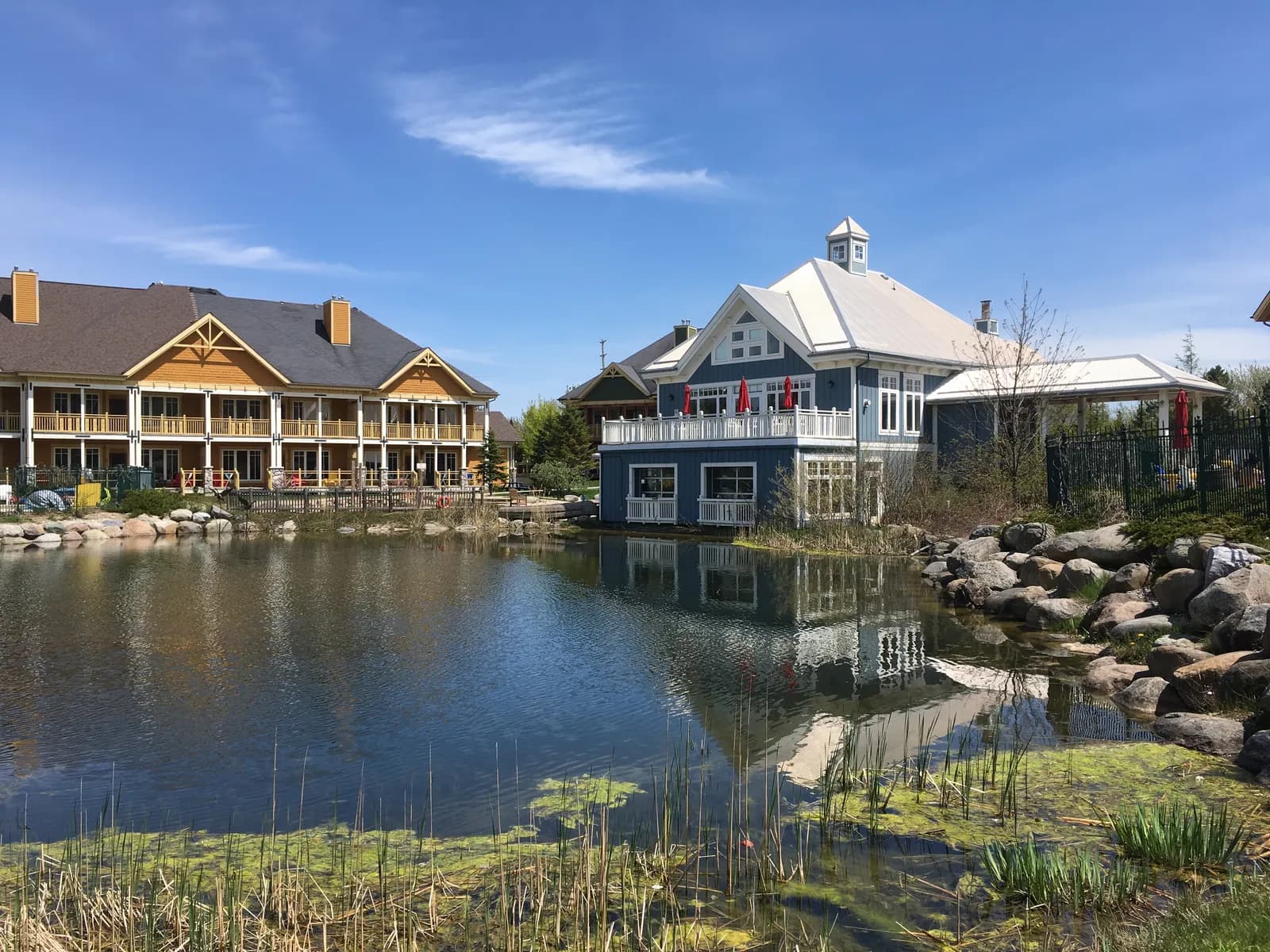 Lodge buildings at Hilton Grand Vacations Club Blue Mountain Canada, their timber balconies and painted siding reflected in the pond in front of them.