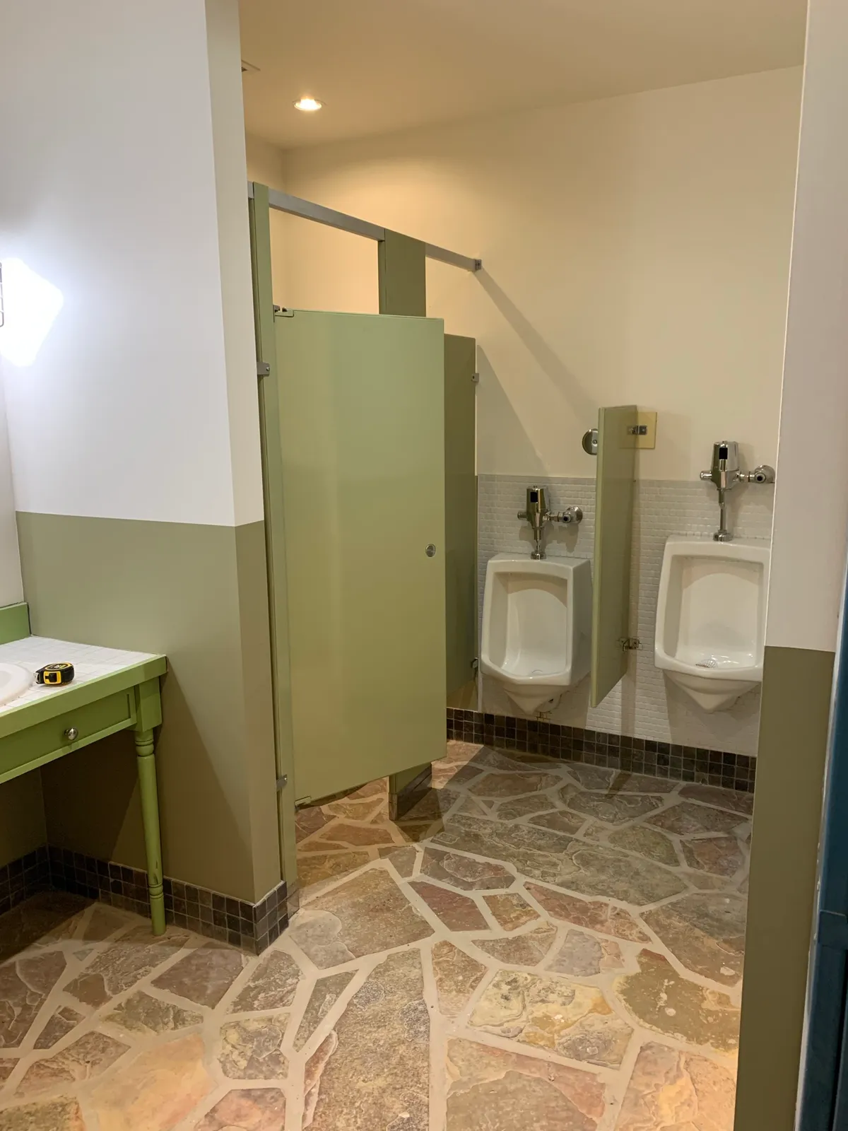 A washroom at Hilton Grand Vacations Club Blue Mountain Canada after repainting, white walls above a sage green lower band, with sage stall partitions and a flagstone floor.