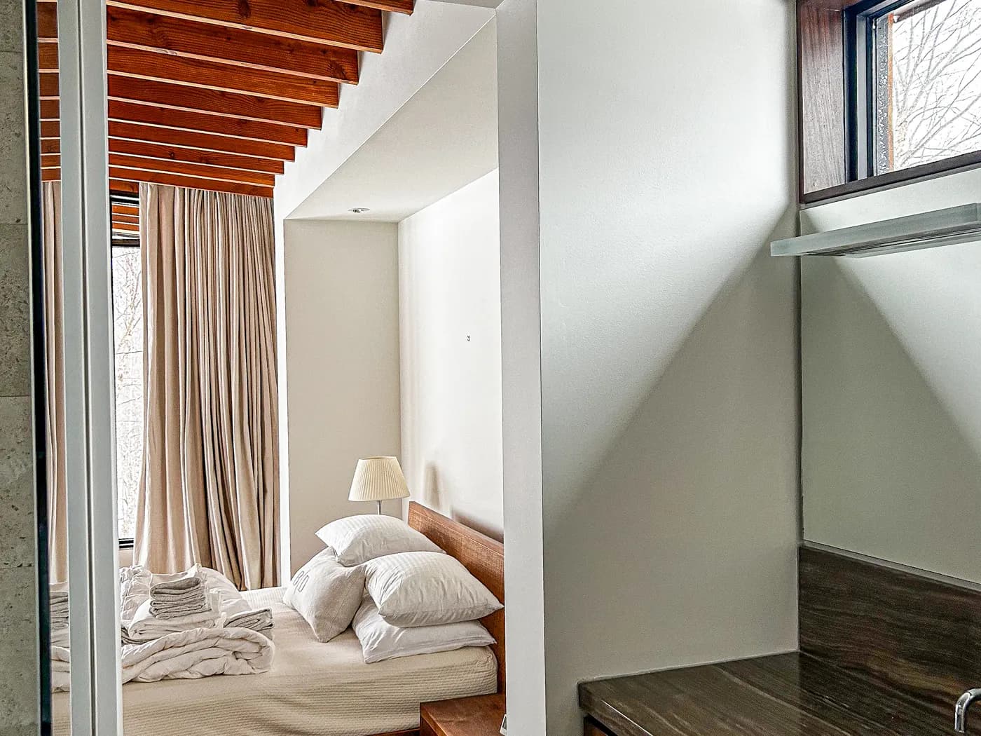 A Clarksburg bedroom under a timber ceiling, its walls painted a soft neutral beside a full height curtain.