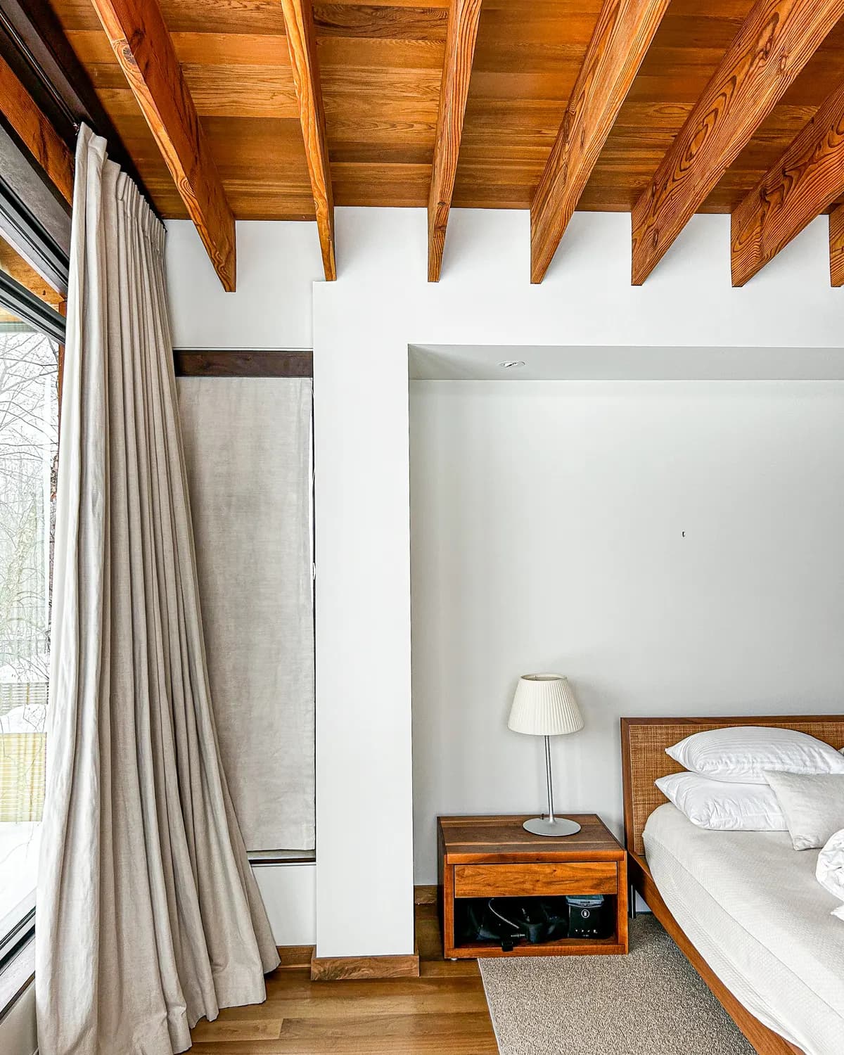 A Clarksburg bedroom beneath exposed timber rafters, its walls painted a warm white beside a full height curtain.