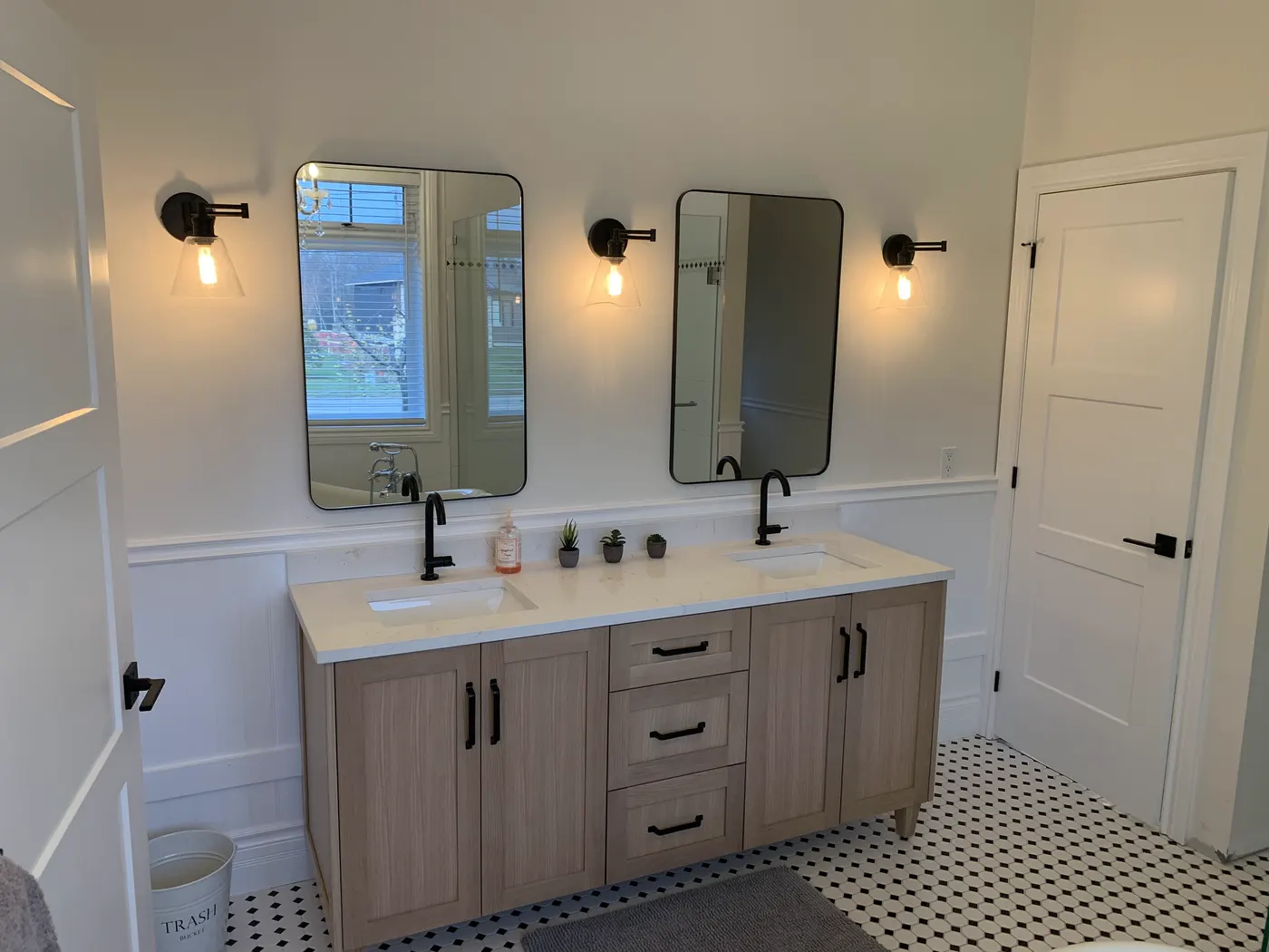 A double vanity beneath two black framed mirrors and wall sconces, with painted walls and panelling either side.