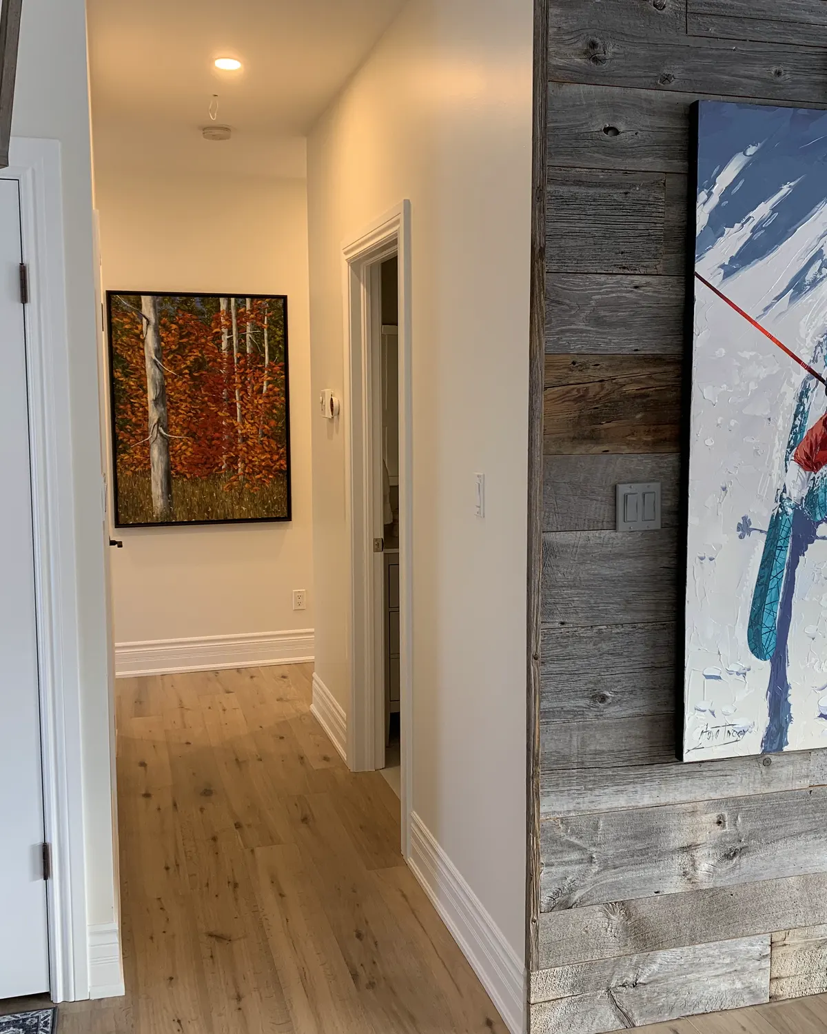 A hallway in a Blue Mountain chalet, freshly painted walls meeting a reclaimed barn board feature wall hung with ski artwork.