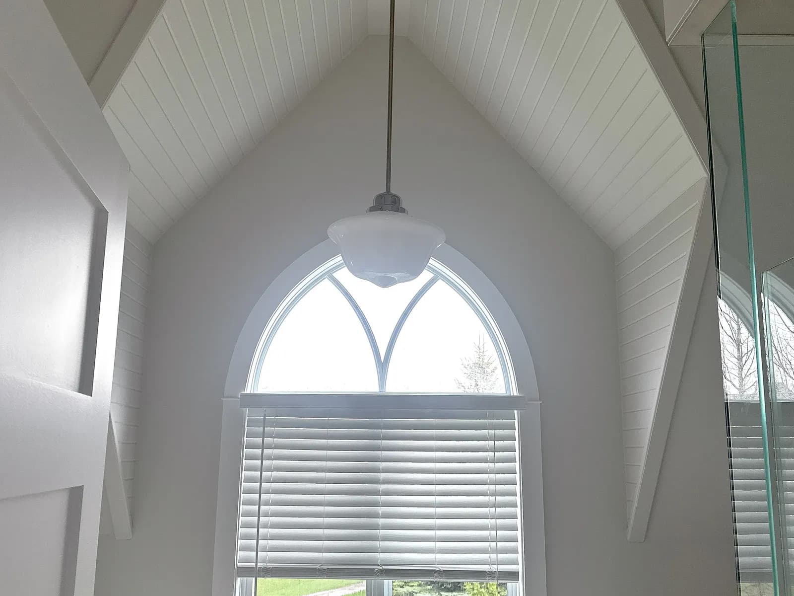 A vaulted ceiling painted white above an arched window in a Snowbridge chalet, with a single pendant hanging from the peak.