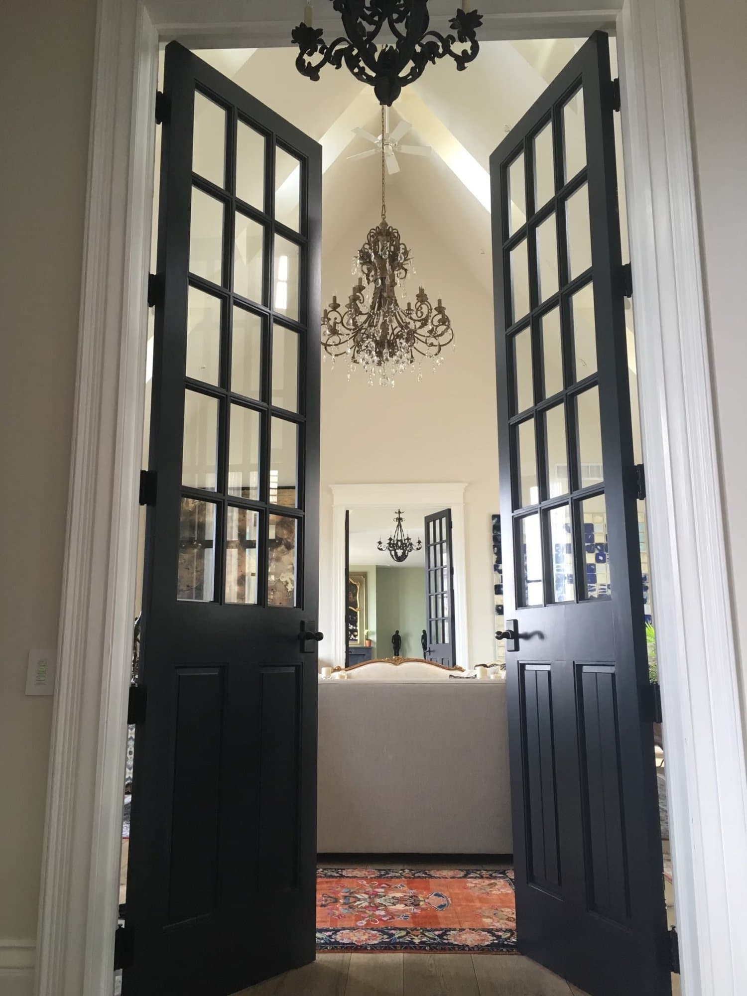 Black painted French doors opening into a bright great room with a vaulted white ceiling and chandelier.