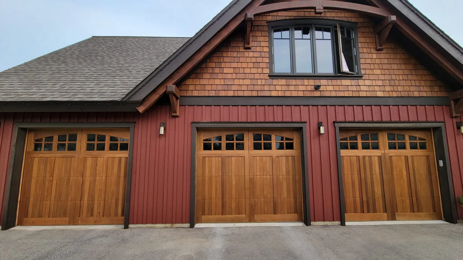 Two wood carriage garage doors on a timber frame home near Markdale, set in deep red board and batten beneath a cedar shake gable.