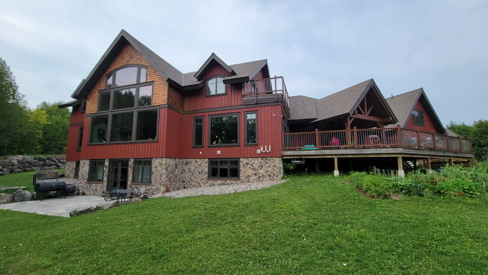 The long elevation of a timber frame home near Markdale in deep red solid stain, its covered deck running above stone footings.
