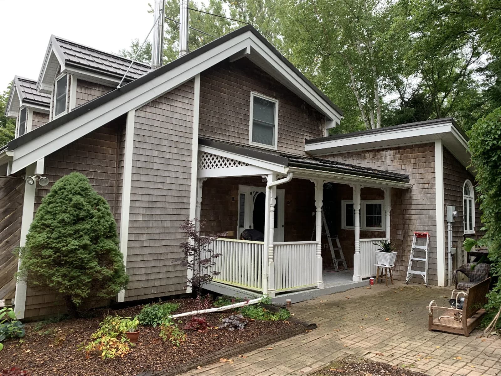 A shingled cottage before painting, its cedar shakes weathered brown and the porch trim dulled.