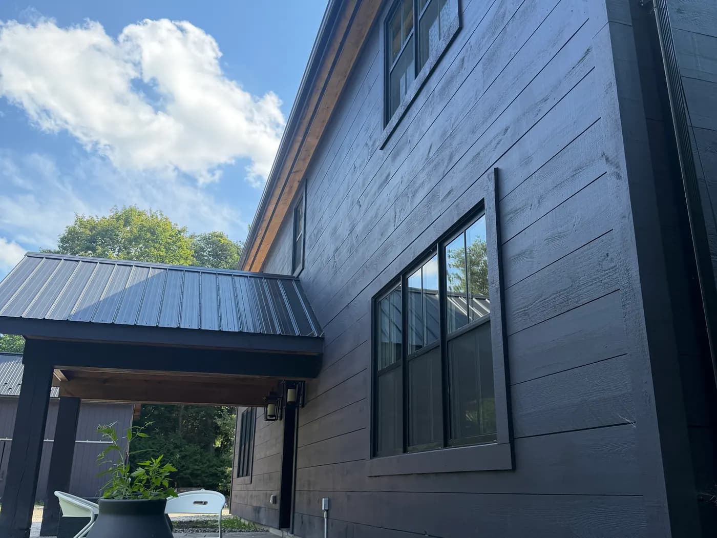 The corner of a Nottawa home where the deep stained siding meets a standing seam roof and a covered entry.