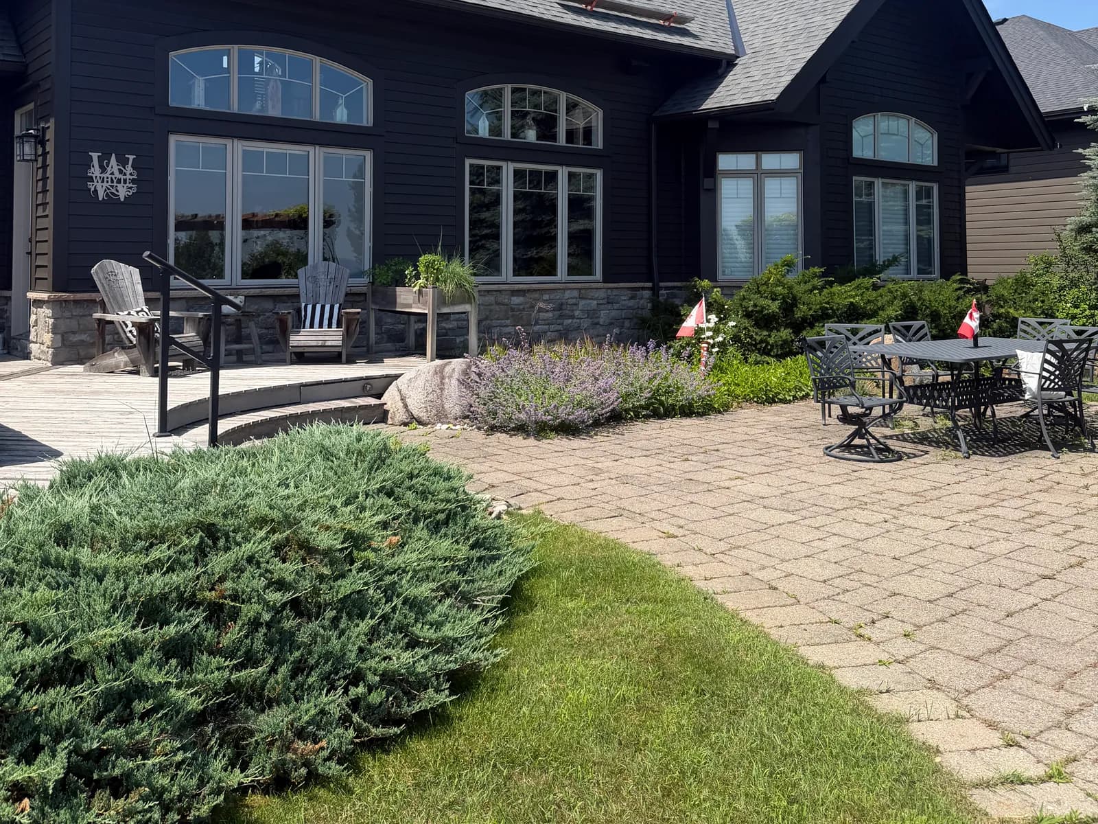 A large Lora Bay home in Thornbury painted a single deep charcoal across siding, trim and soffits, with a stone patio and Muskoka chairs under a clear sky.