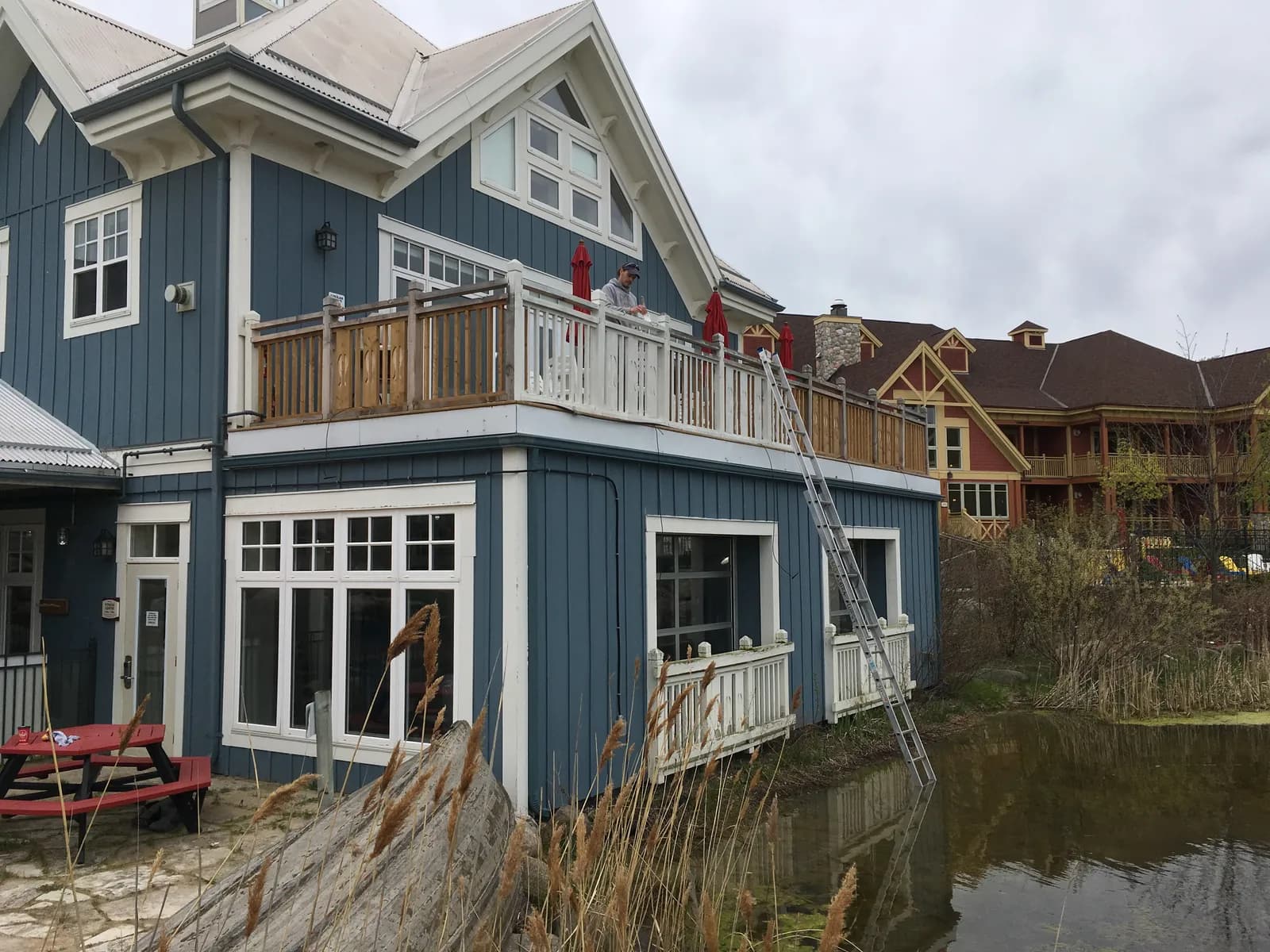 A two storey lodge building at Hilton Grand Vacations Club Blue Mountain Canada, painted navy with white trim and balcony rails, its lawn running down to the pond.