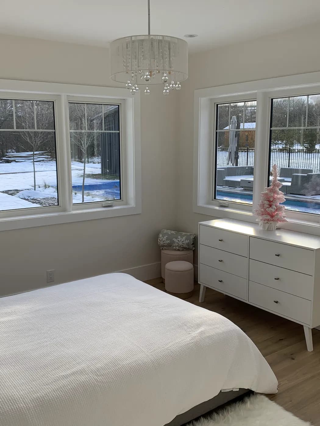 A bedroom painted in a soft warm white, with two windows onto a snowy garden and a beaded pendant light overhead.