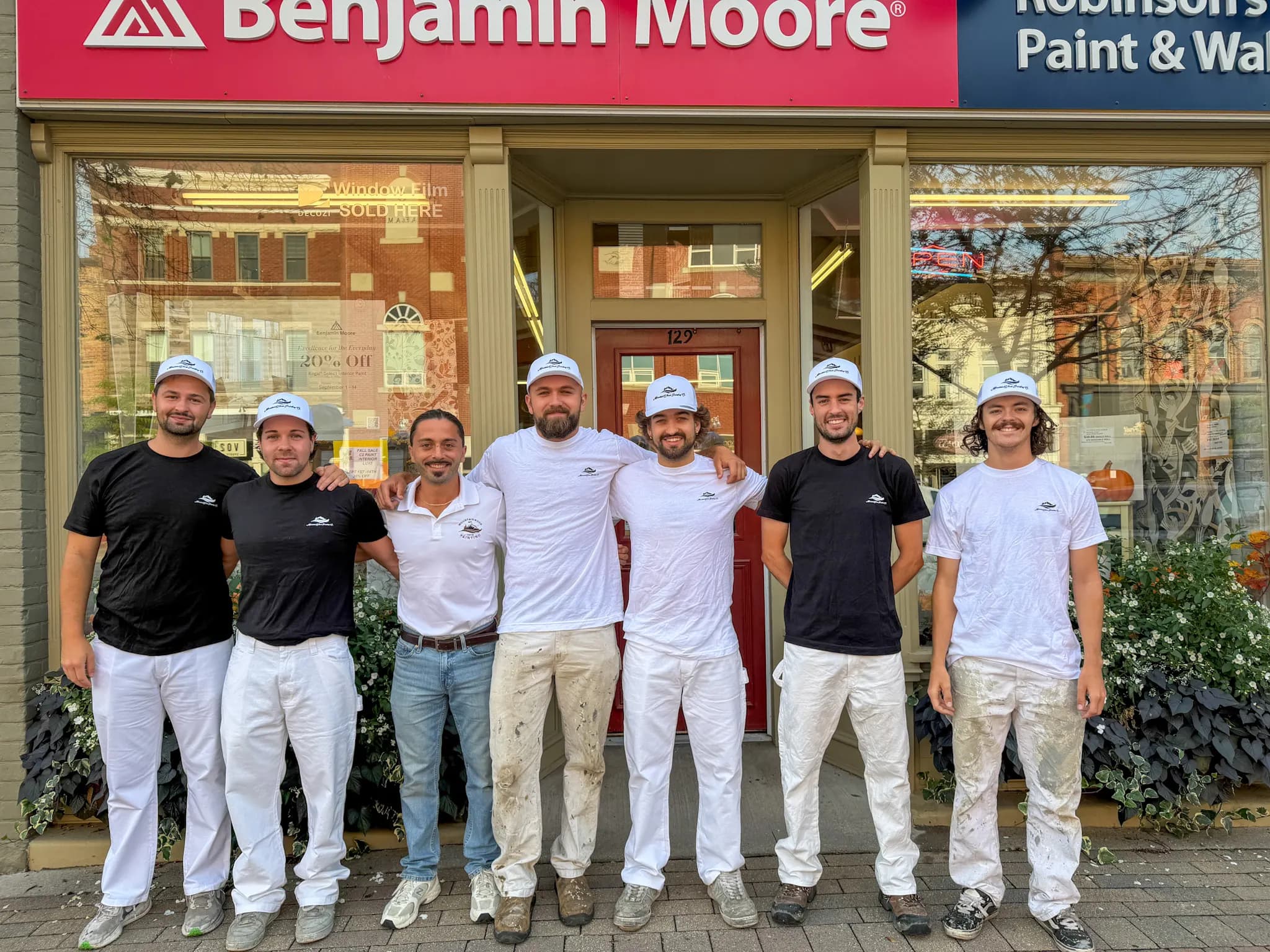 The MountainWood Painting crew outside a Benjamin Moore paint store, in branded shirts, caps and painters' whites.